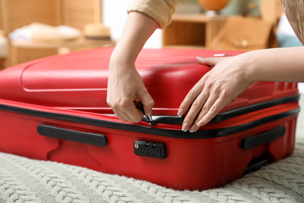 Hands zipping up a large red suitcase